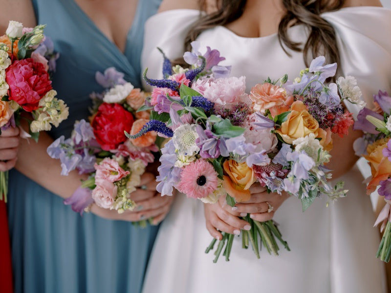 Bride and bridesmaids holding colorful floral bouquets.