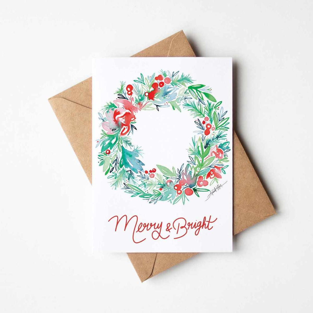 Amanda Klein Co. | Merry & Bright Notecard Stationery Set | A white card with a watercolor wreath on the front and text that reads "Merry & Bright". Comes with a kraft brown envelope.