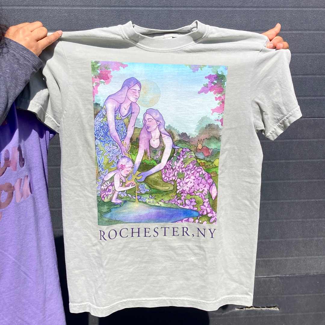 Andrea Durfee | Lilac Goddess T-Shirt | A bay green comfort colors t shirt with Andrea Durfee's Lilac Goddess piece printed on top. Text underneath reads "Rochester, NY".