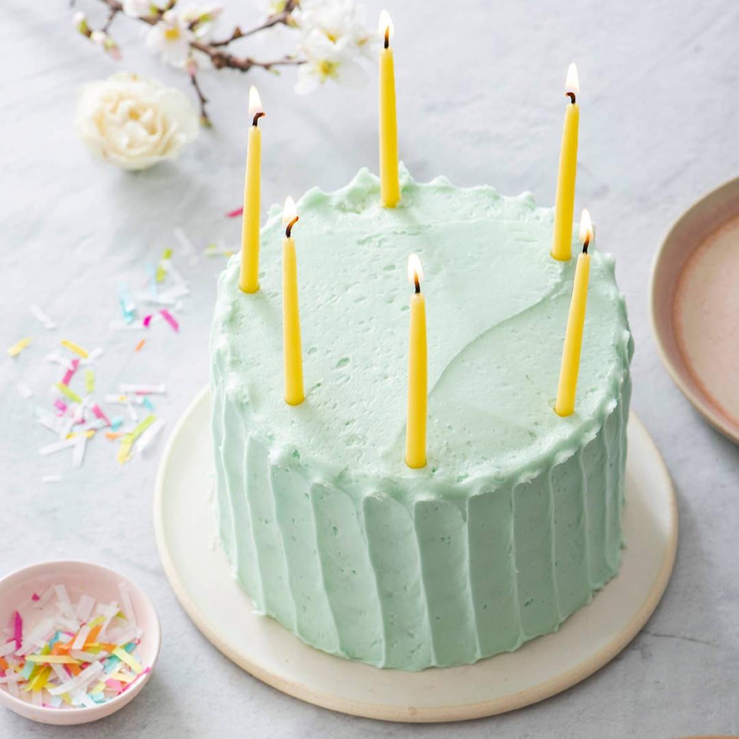 Anellabees | Beeswax Candles | Green frosted cake with lit candles on a light gray surface with decorative elements.