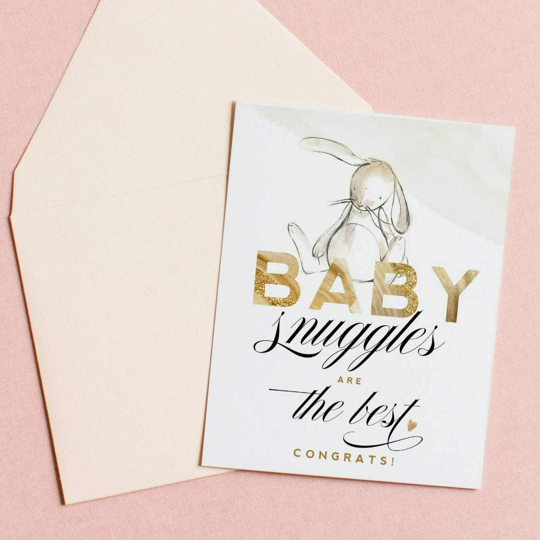 A white card with a watercolor style bunny rabbit and text that reads "Baby snuggles are the best, congrats!". in gold and black.