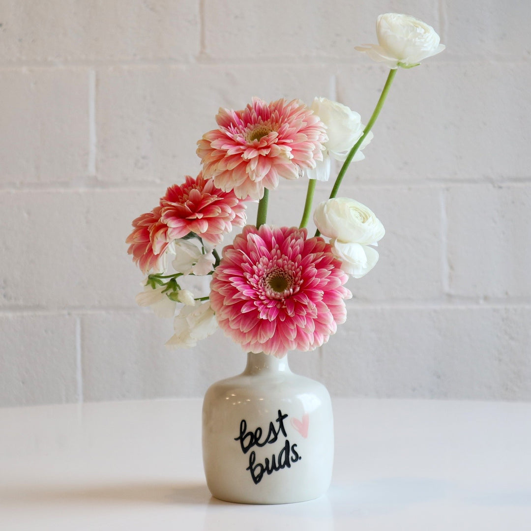 Best Buds | A vased arrangement in a white vase that reads " Best Buds" with a pink heart. Florals are pink and white. Photo taken against a white background.