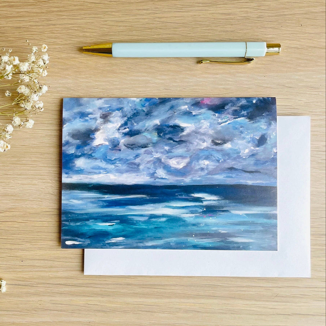 Beth Garner | Stacy K Floral | Greeting card with ocean and cloud design on a wooden surface with flowers and pen.