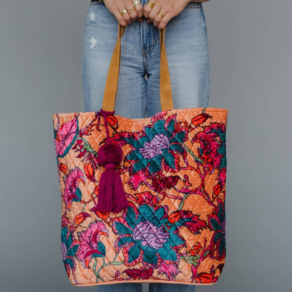 Person holding a colorful floral tote bag with a gray background
