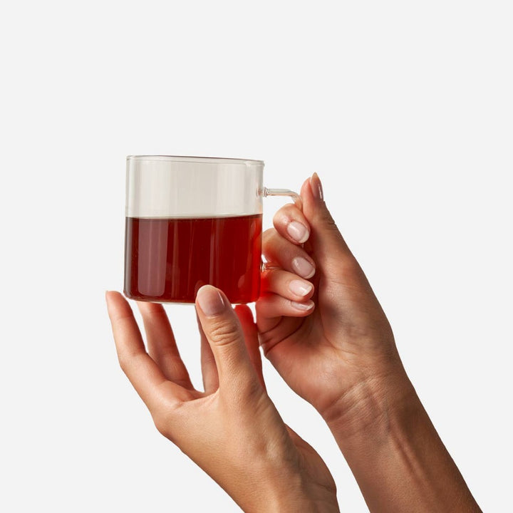 Big Heart Tea | Hands holding a clear mug with red liquid against a white background