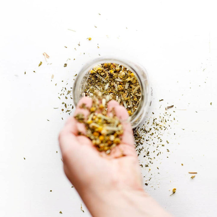 Big Heart Tea Co | Hand holding dried tea above a glass jar on a white background