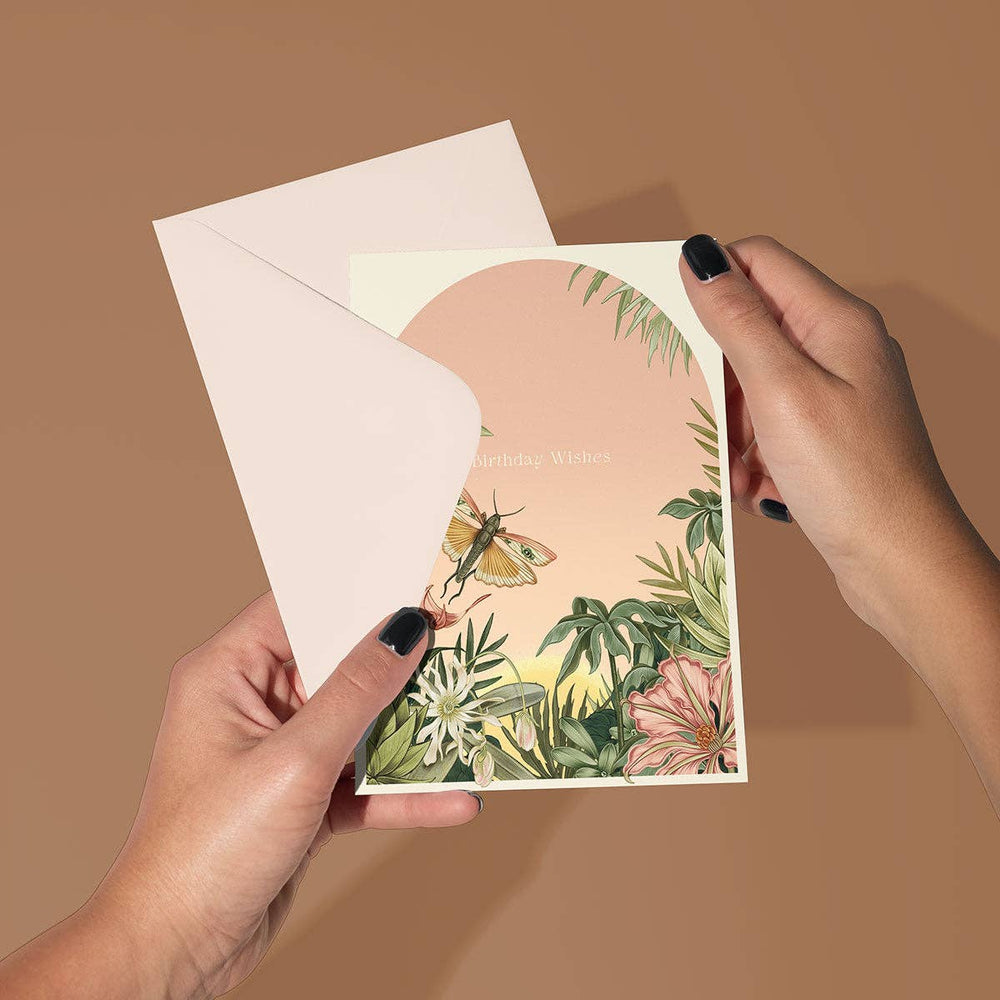 Hand holding a card with floral and butterfly design against a brown background