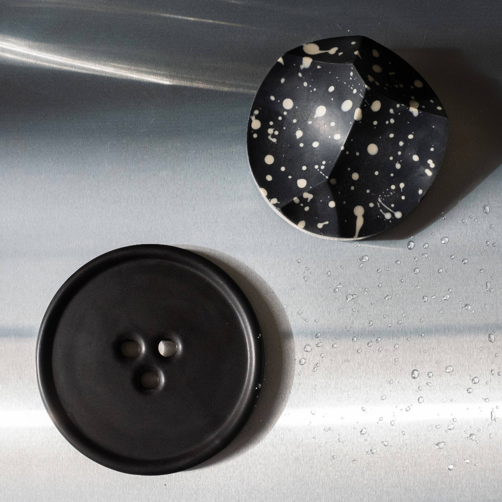 Two buttons, one black and one with a speckled pattern, on a metallic surface.