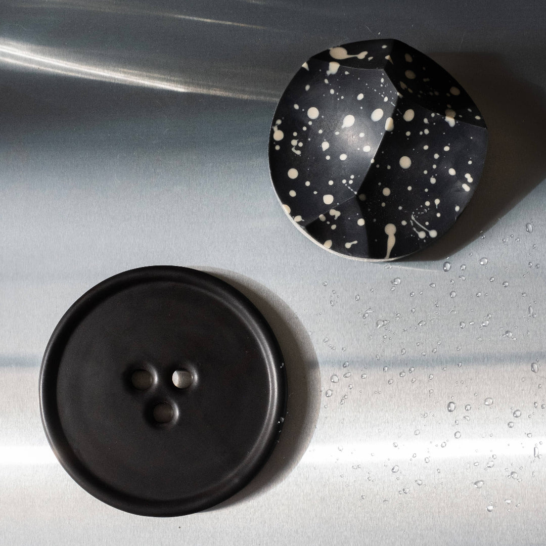 Two buttons, one black and one with a speckled pattern, on a metallic surface.