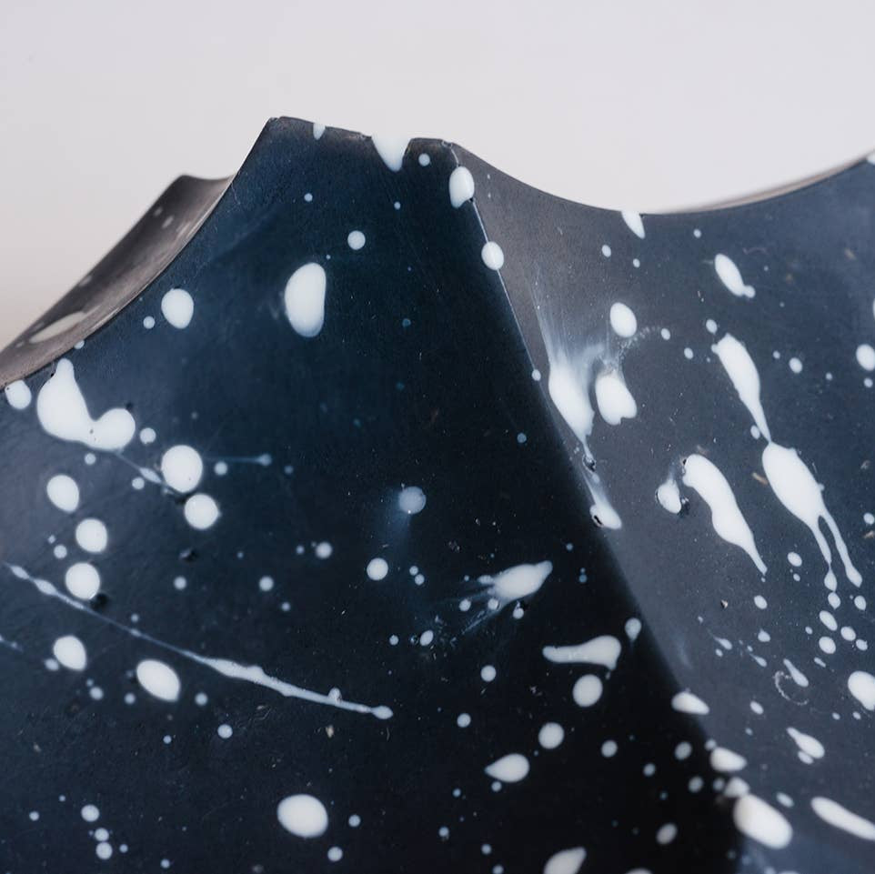Ceramic plate with black glaze and white speckles on a light gray background