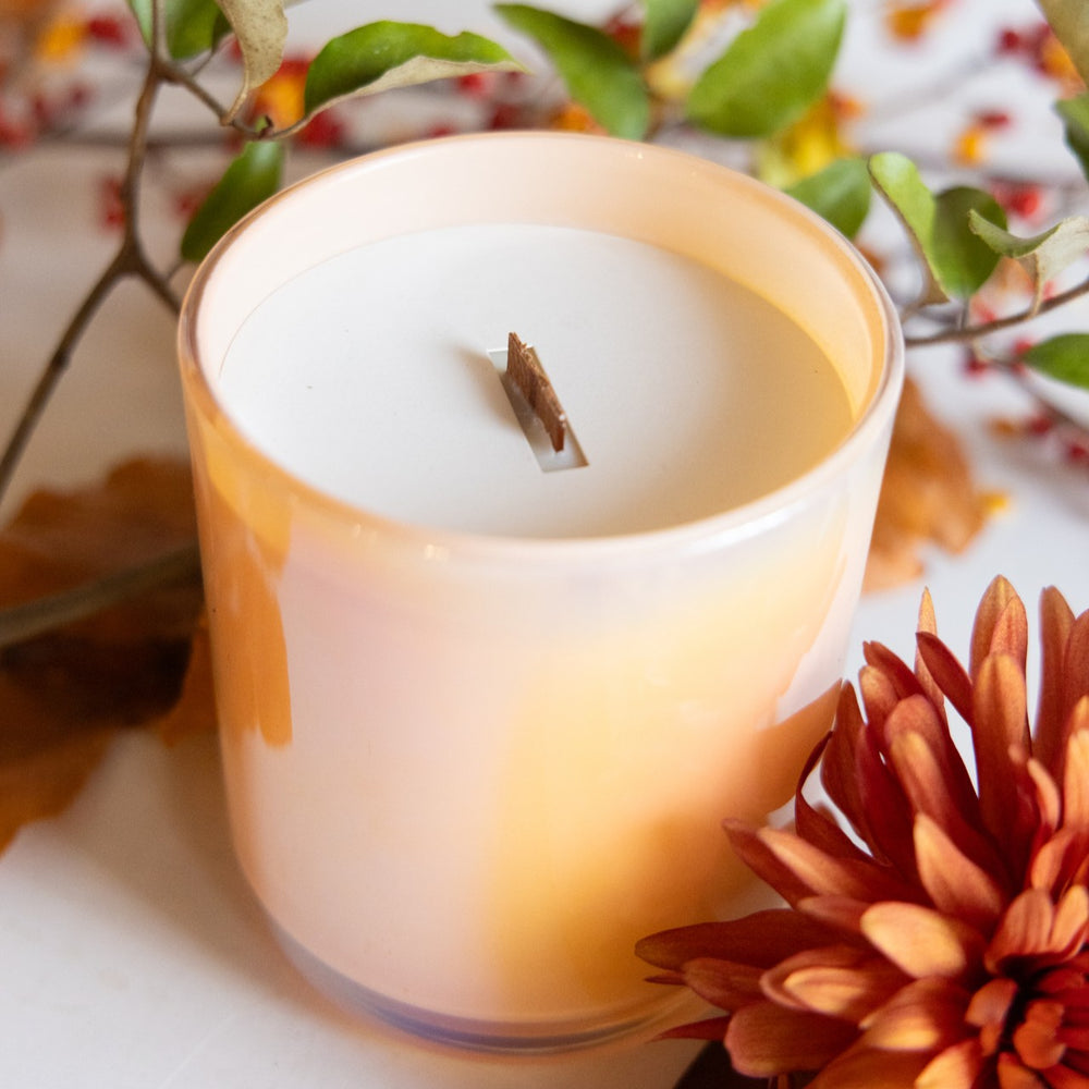 Candle in a glass holder with autumn decorations including leaves and flowers.