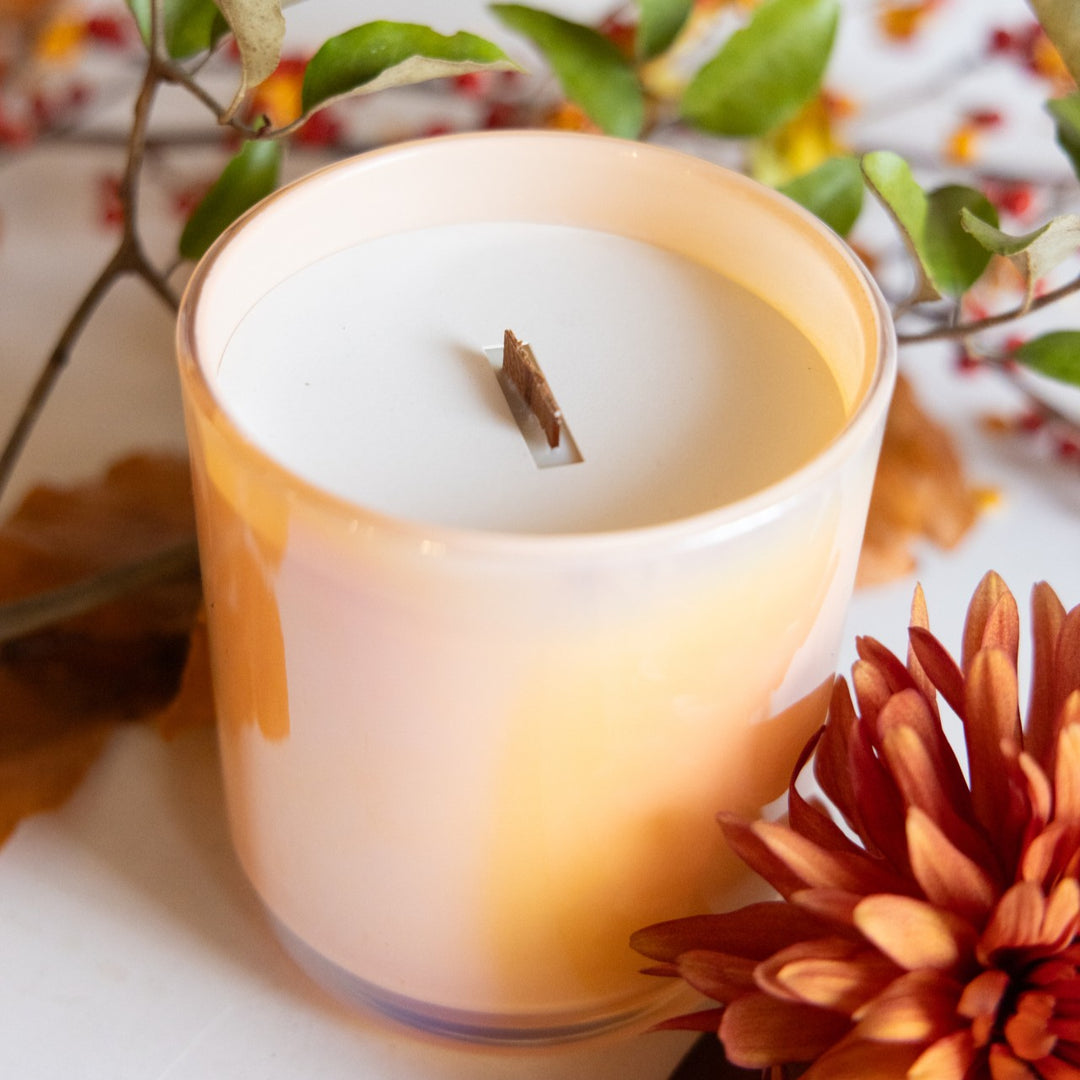 Candle in a glass holder with autumn decorations including leaves and flowers.