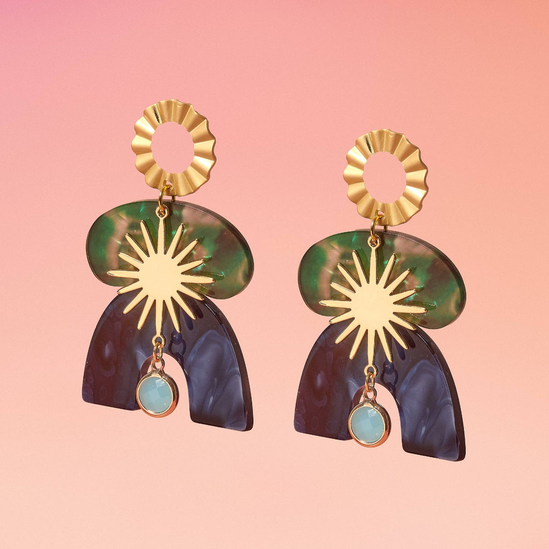 Pair of earrings with gold, green, and blue design on a pink background