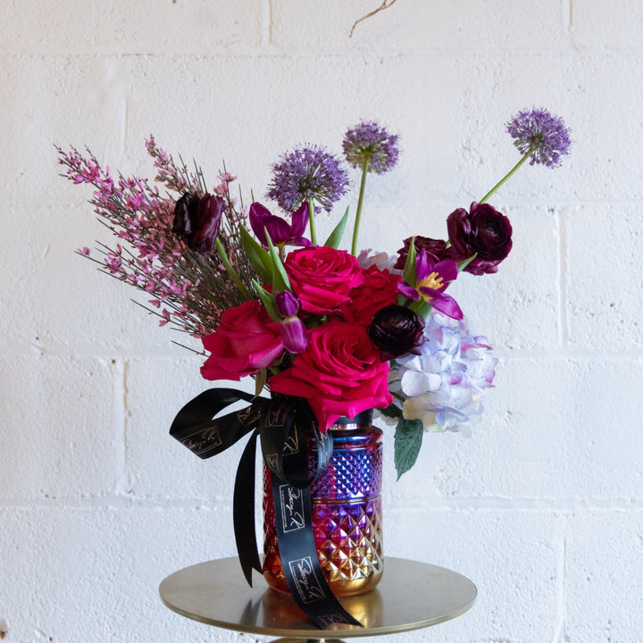 Colorful flower arrangement in a decorated glass jar on a white brick wall background