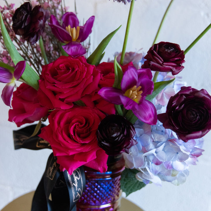 Bouquet of red and purple flowers in a textured vase on a white background