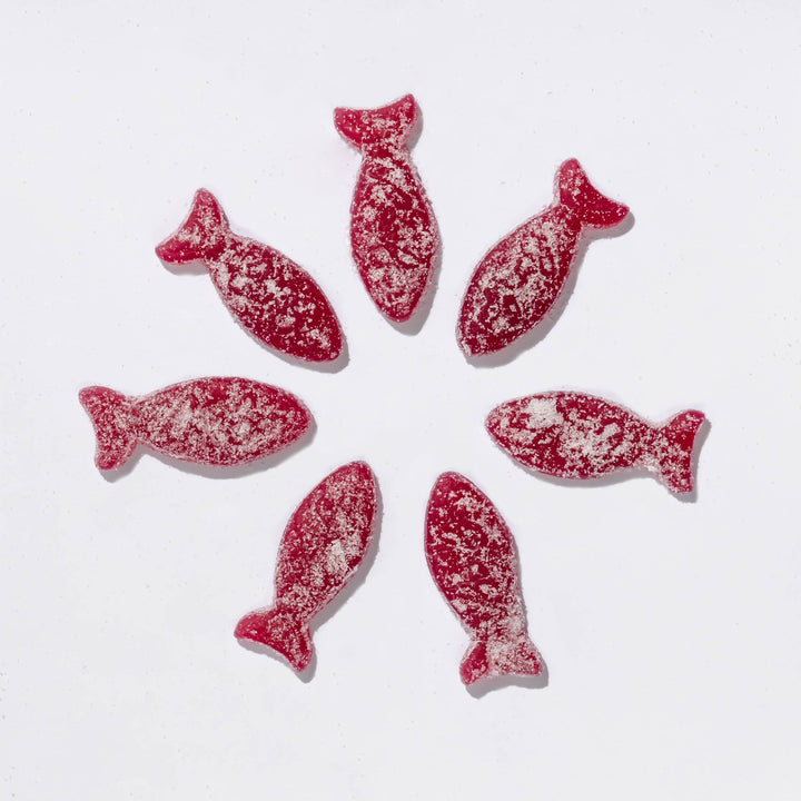 Red fish-shaped candies with white sprinkles on a white background