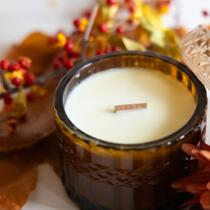 Candle in a decorative glass jar with autumn-themed elements in the background
