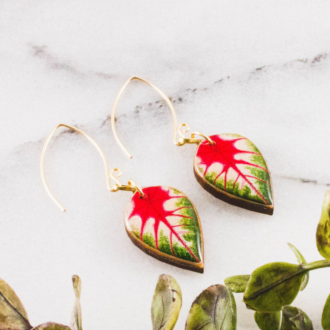 Pair of leaf-shaped earrings with red and green design on a marble surface.