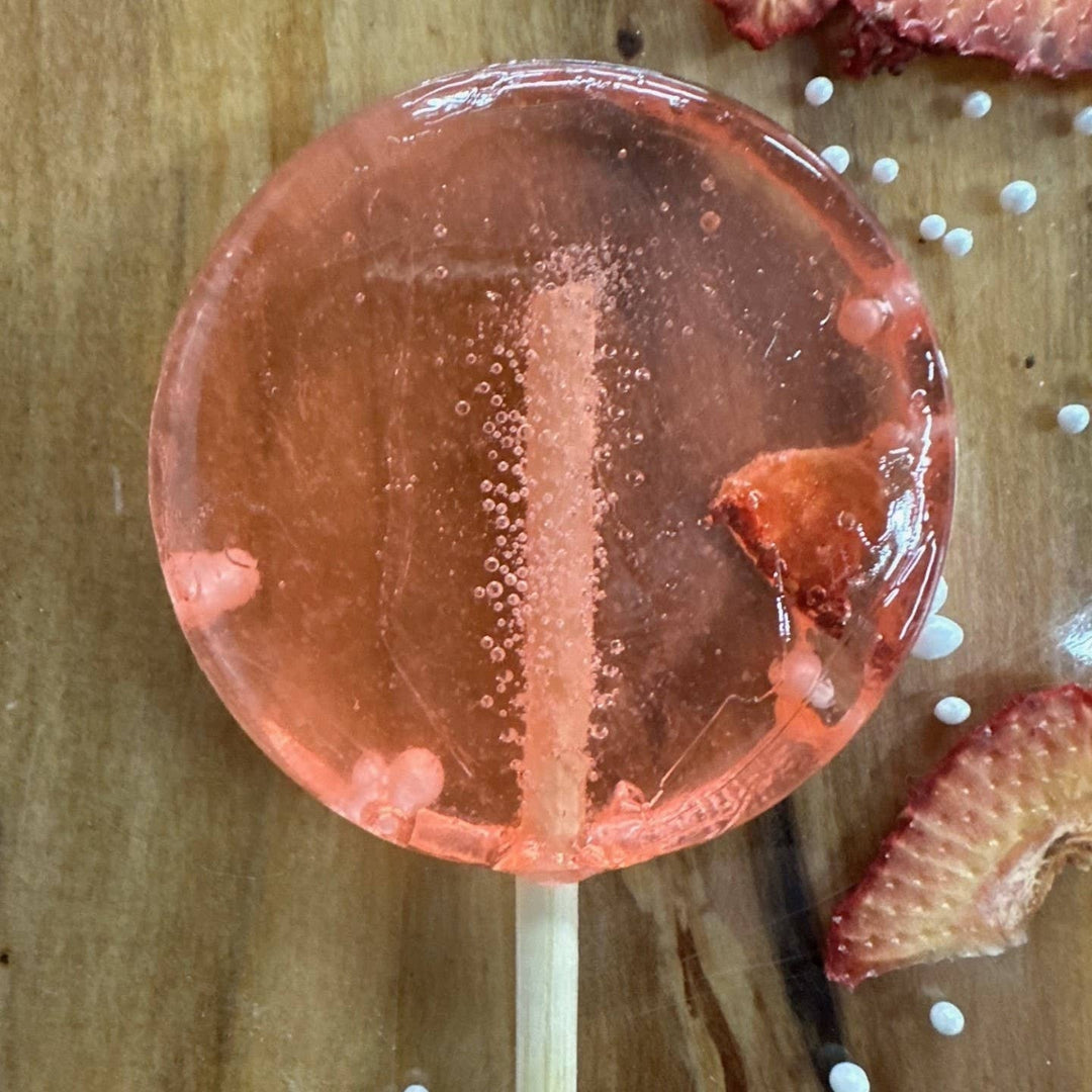 Pink lollipop on a wooden surface with dried strawberries and white pearls.