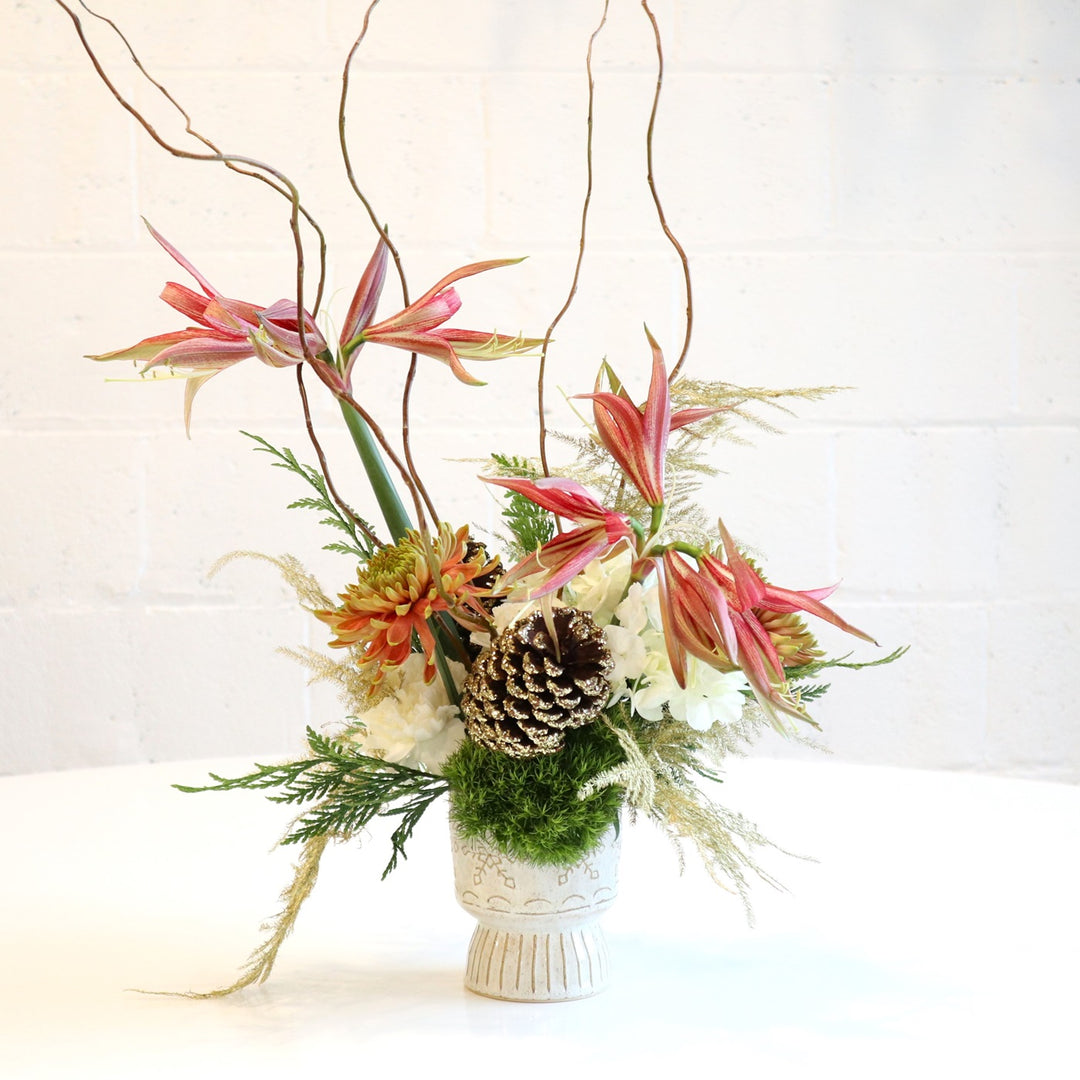 Christmas Spice | An elegant vased arrangement with lilies, mums, hydrangea, moss, and branching. Created in a white vase. Photo taken against a white background.