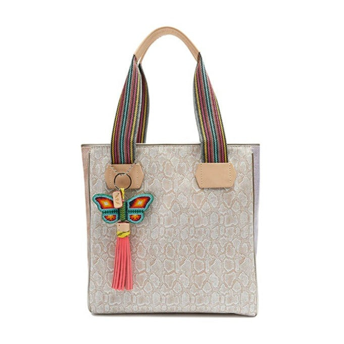 Clay Classic Tote | Consuela | A nude/gray colored tote bag with multi colored straps, Diego leather accents, and a colorful butterfly charm.