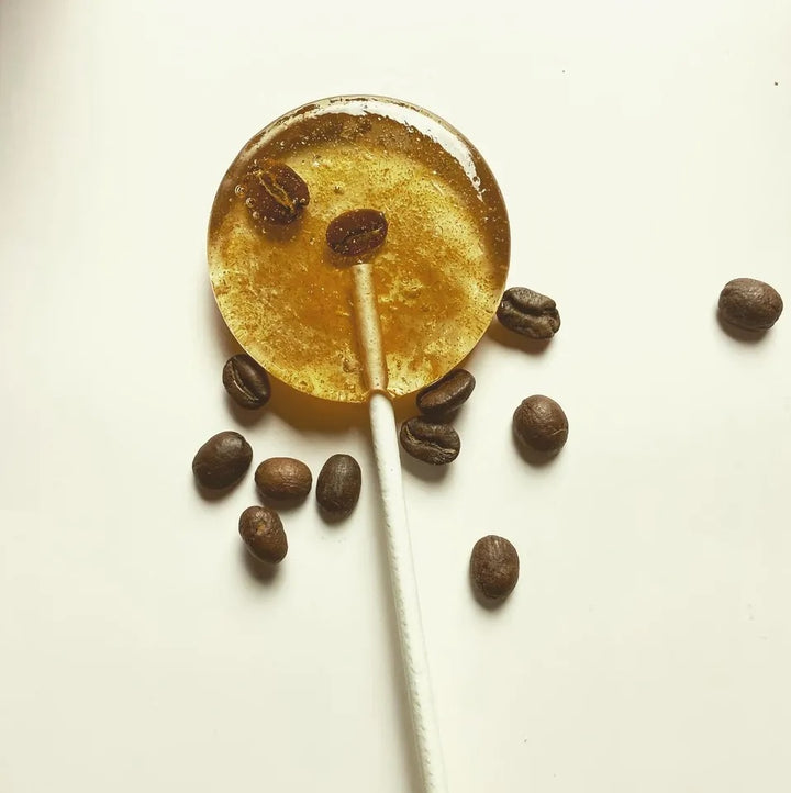 Good Lolli Lollipops | Coffee | A transparent lolli with coffee beans inside. Photo taken against a white background with coffee beans placed about.