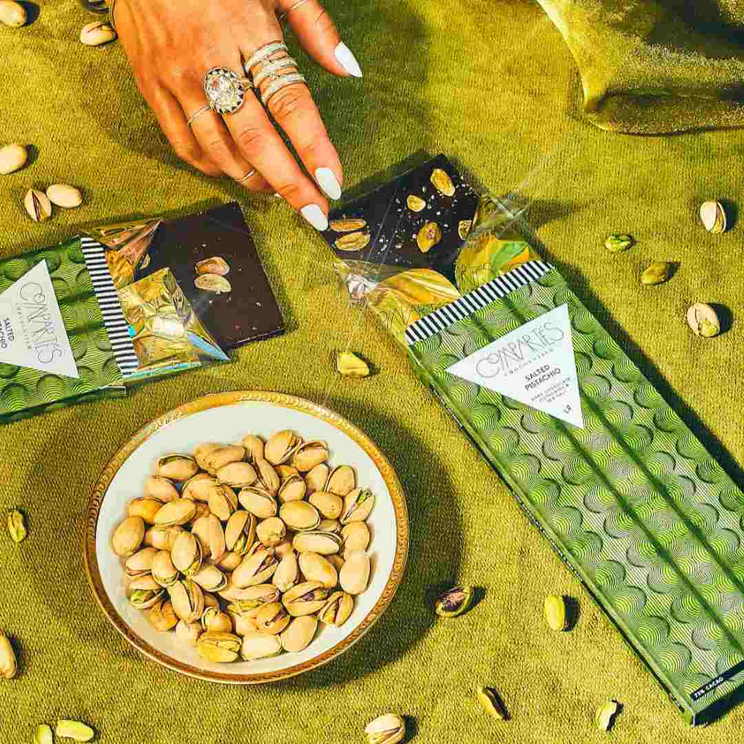 Compartes Chocolate | Salted Pistachio Dark Chocolate Bar | A green package on a green cloth with decorative pistachios placed around.