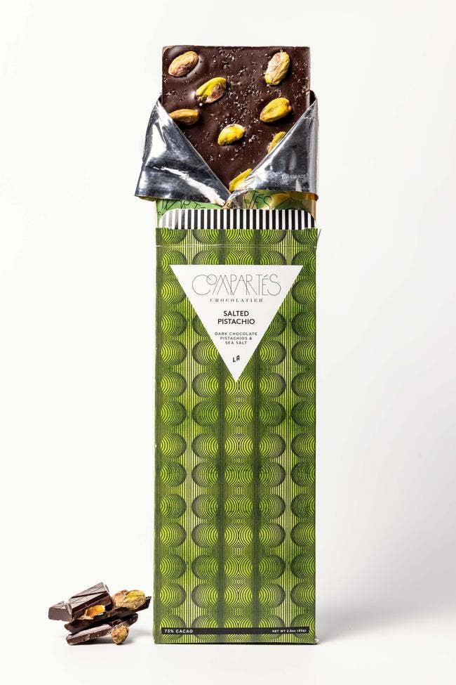 Compartes Chocolate | Salted Pistachio Dark Chocolate Bar | A green package with the chocolate sticking out the top. Whole sized pistachios can be seen.