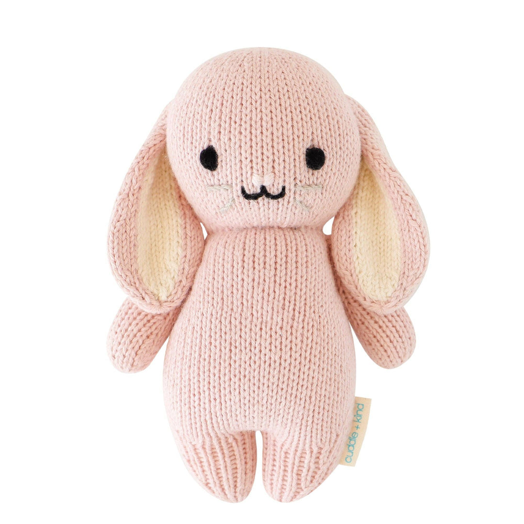 Knitted pink bunny toy with a small tag on a white background