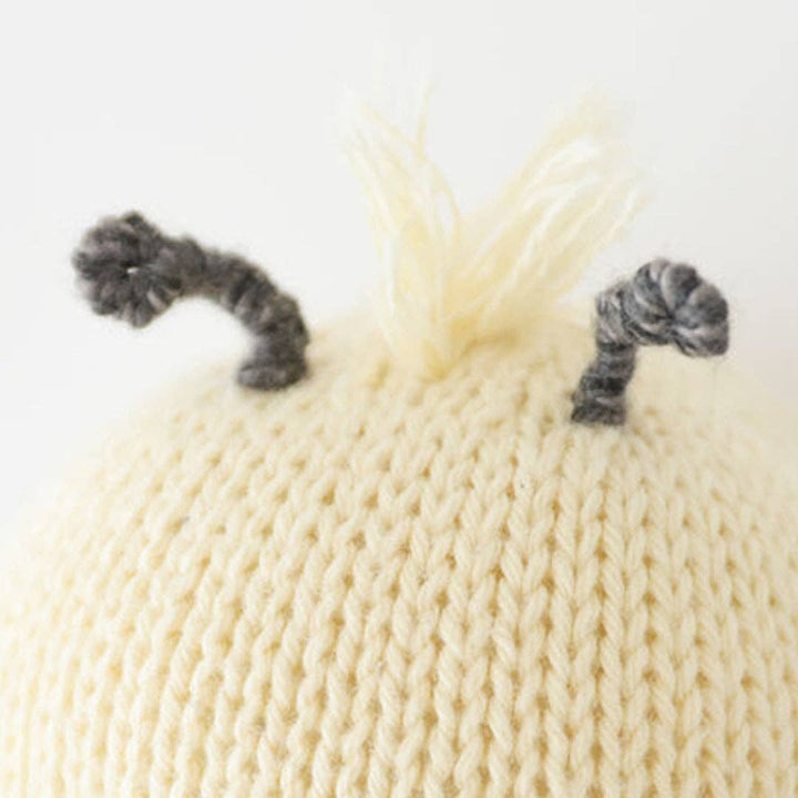 Close-up of a cream-colored knitted hat with gray pom-poms on a white background