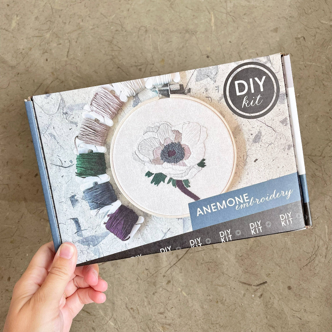 DIY embroidery kit packaging with anemone design on a textured surface