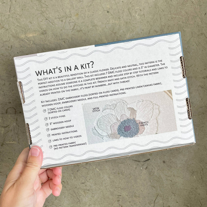 Hand holding a DIY embroidery kit with text and flower illustration on a textured surface