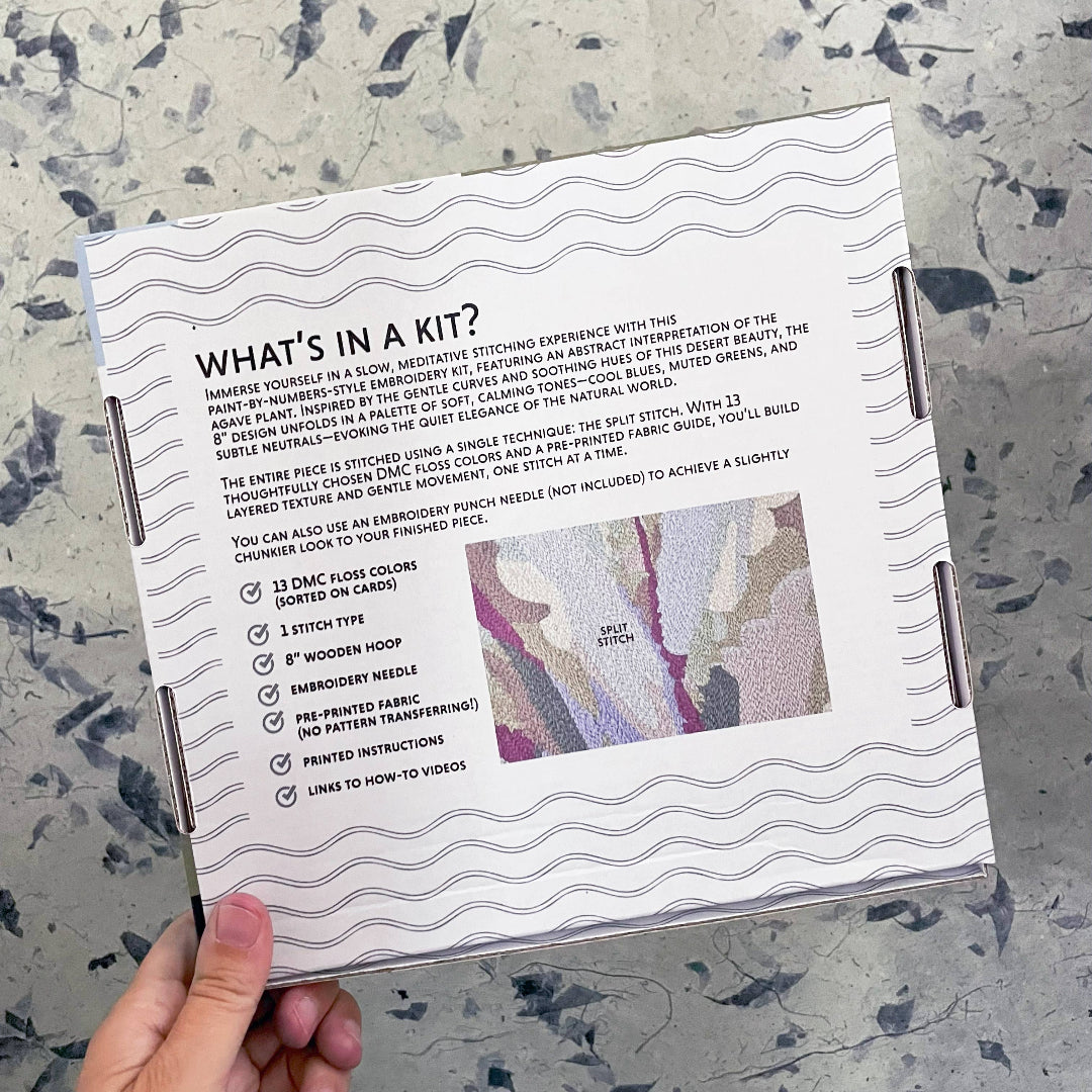 Embroidery kit packaging with text and fabric sample on a textured surface