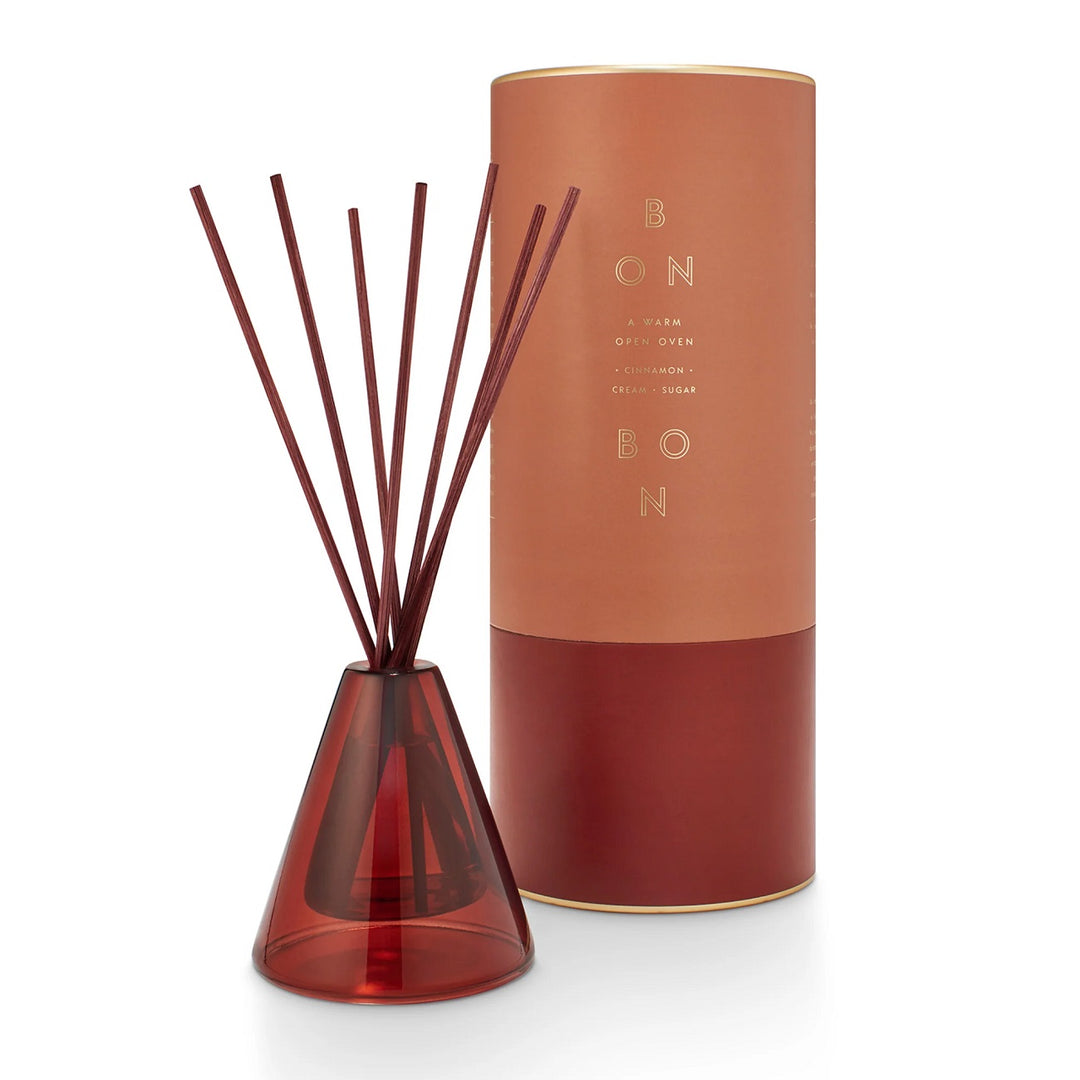 Winsome Diffuser | Bon Bon, a warm open oven, cinnamon, cream, and sugar scented. A tapered diffuser with the scent carrying sticks sticking out. The diffuser is a dark red-ish color.