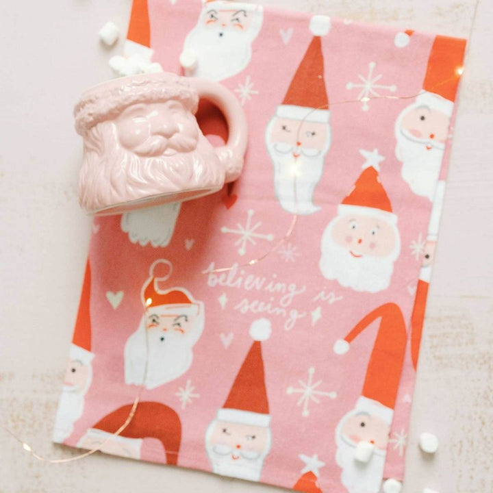 Doe A Deer | Believing Is Seeing Santa Full Pattern Towel | A santa claus patternd towel with text "believing is seeing" on a pink background.