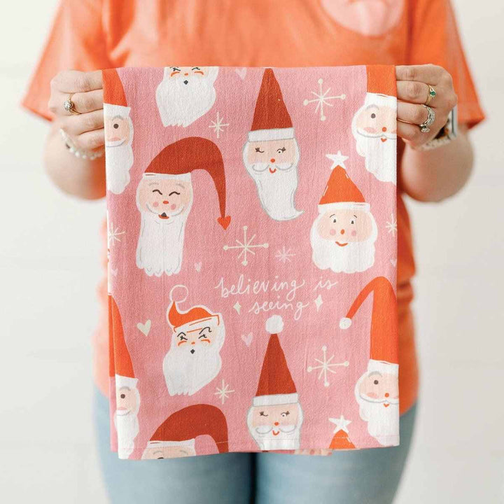 Doe A Deer | Believing Is Seeing Santa Full Pattern Towel | A santa claus patternd towel with text "believing is seeing" on a pink background.