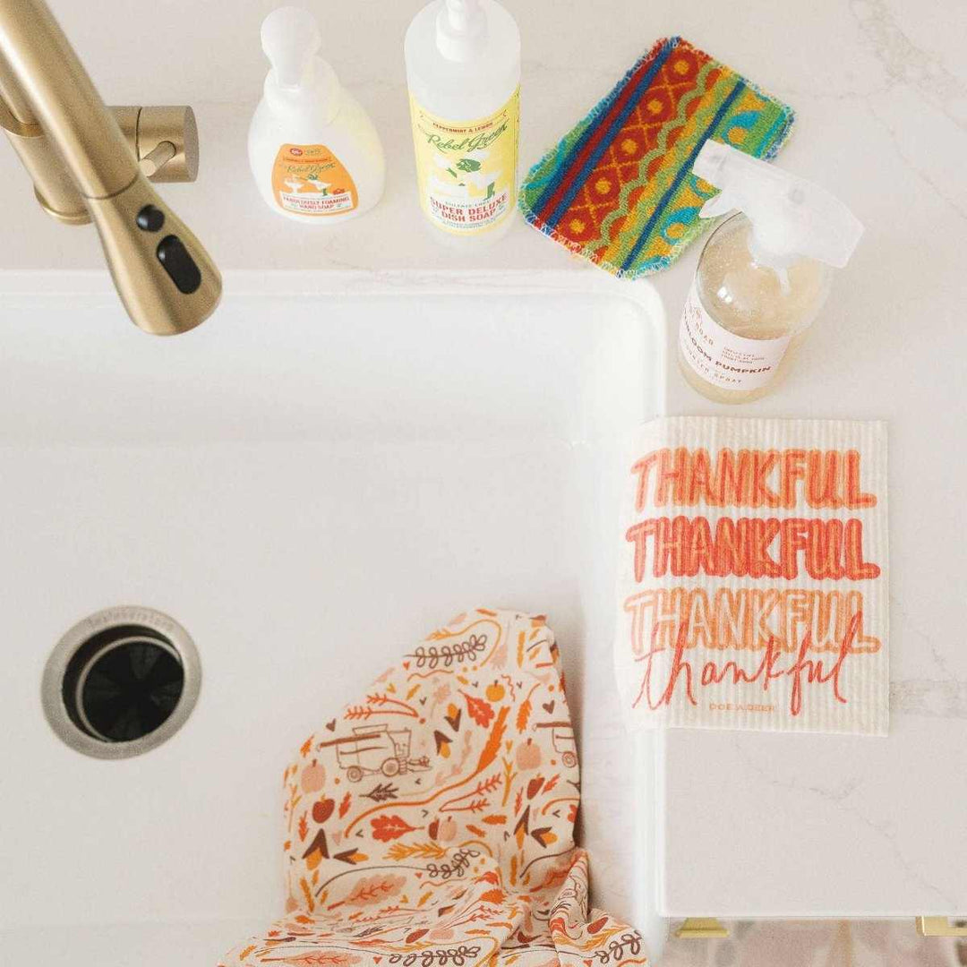 Doe A Deer | Thankful Swedish Dishcloth | a white cloth with orange text that reads "Thankful thankful thankful thankful". Draped on the sde of a sink.