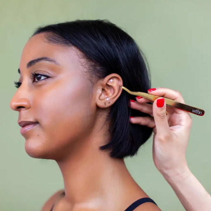 Woman using tweezers to apply the ear seeds against a plain background