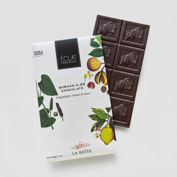 A package of Éclat Chocolat Borneo N.26 chocolate bar shown next to a dark chocolate bar with embossed cacao pods, on a light gray background.