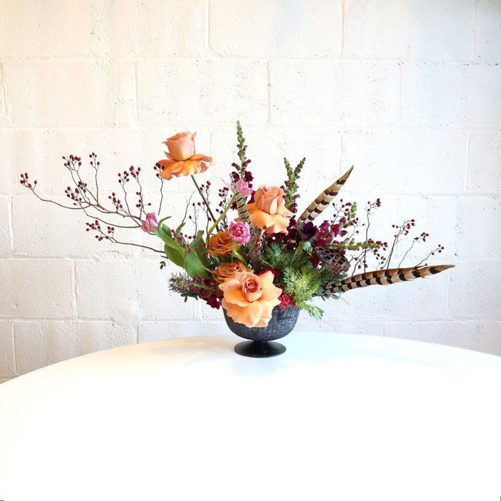 Enchanted | A stunning centerpiece with berries, roses, tulips, feathers, and other florals in the peach/red/green/natural, color palette. Photo taken against a white background.