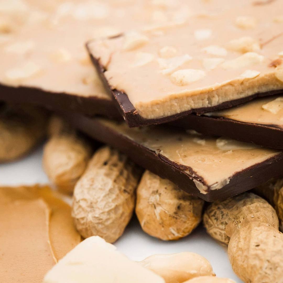 Ethereal Confections | Close-up of a stack of chocolate-covered peanut butter bars with peanuts in the shell.