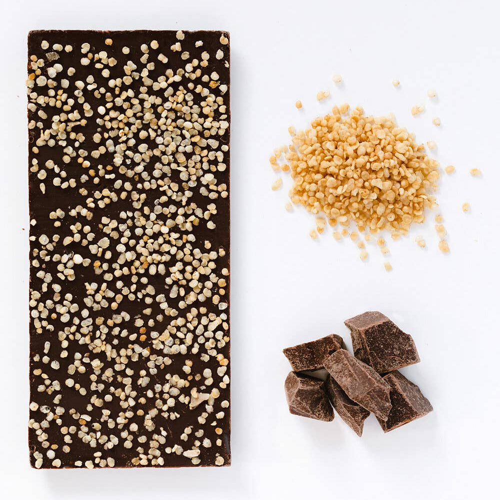 Chocolate bar with gold sprinkles, chopped chocolate pieces, and a small pile of gold beads on a white background