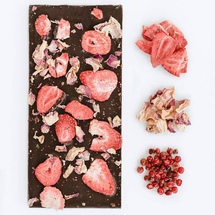 Dark chocolate bar with strawberry pieces and dried flowers on a white background