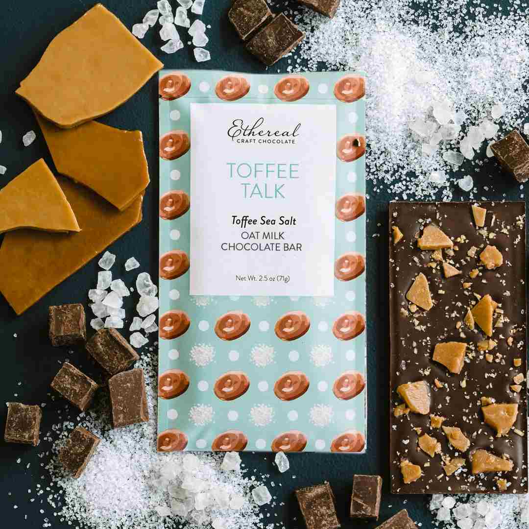 Ethereal Confections | Toffee Talk chocolate bar with toffee pieces and salt on a dark surface. Toffee sea salt, oat milk chocolate bar.