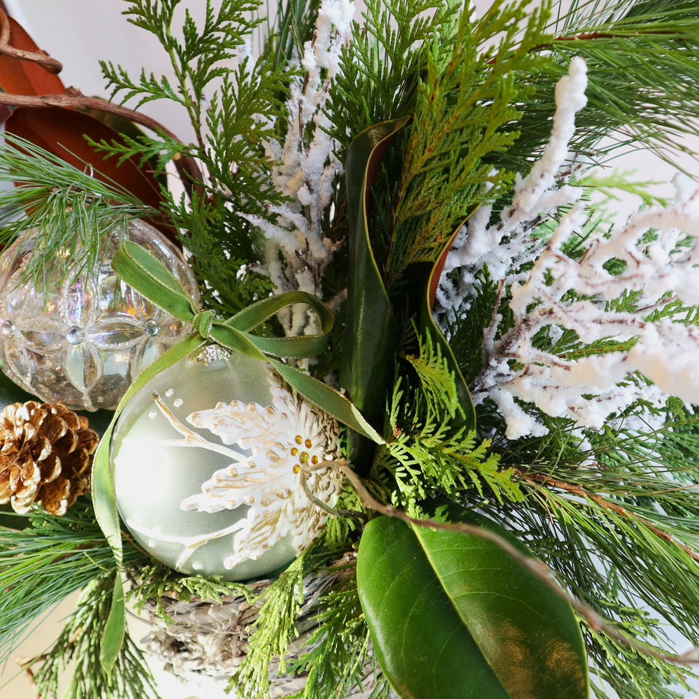 Evergreen Nest Centerpiece | Close up on the glass ornaments, evergreen, flocked branching, and magnolia.