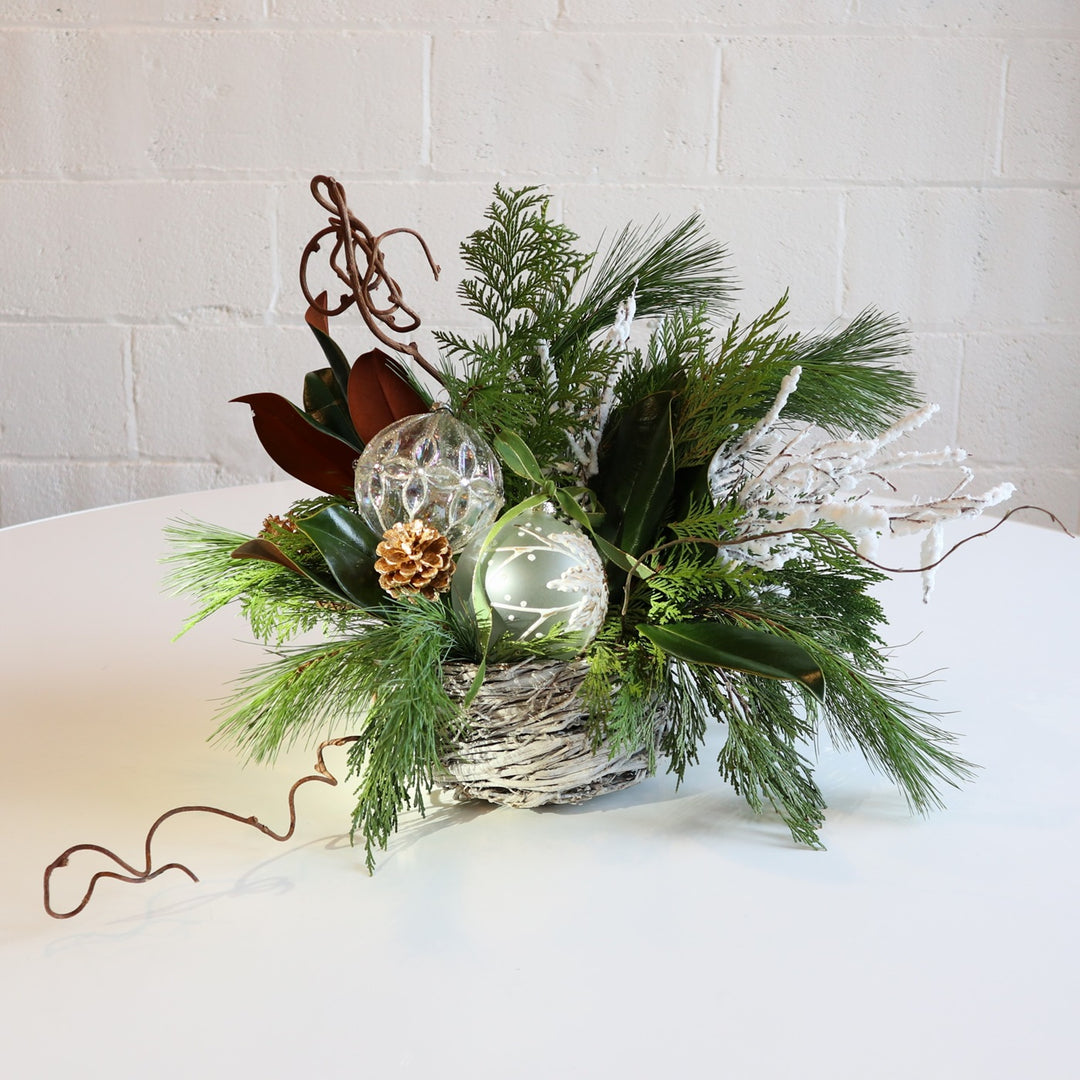 Evergreen Nest Centerpiece | An evergreen arrangement with glass ornaments, branching, and magnolia.