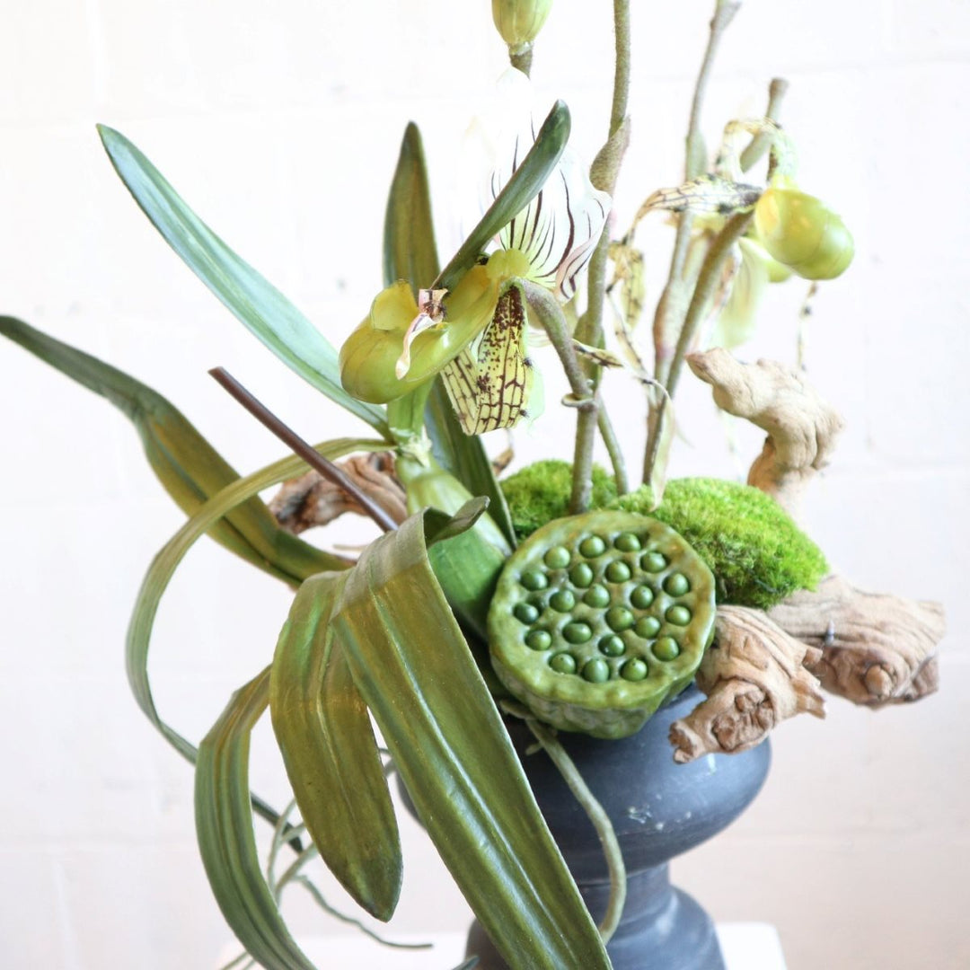 Faux flower arrangement with grapewood, lotus pods, lady slipper orchids, moss in a black vessel.