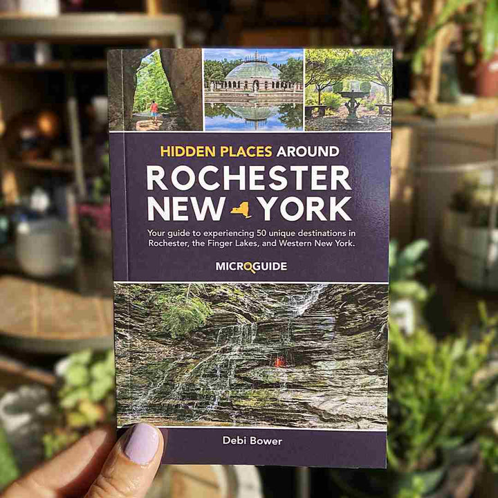 Stacy K Floral | Book titled 'Hidden Places Around Rochester New York' held by a hand with a blurred background. By Debi Bower