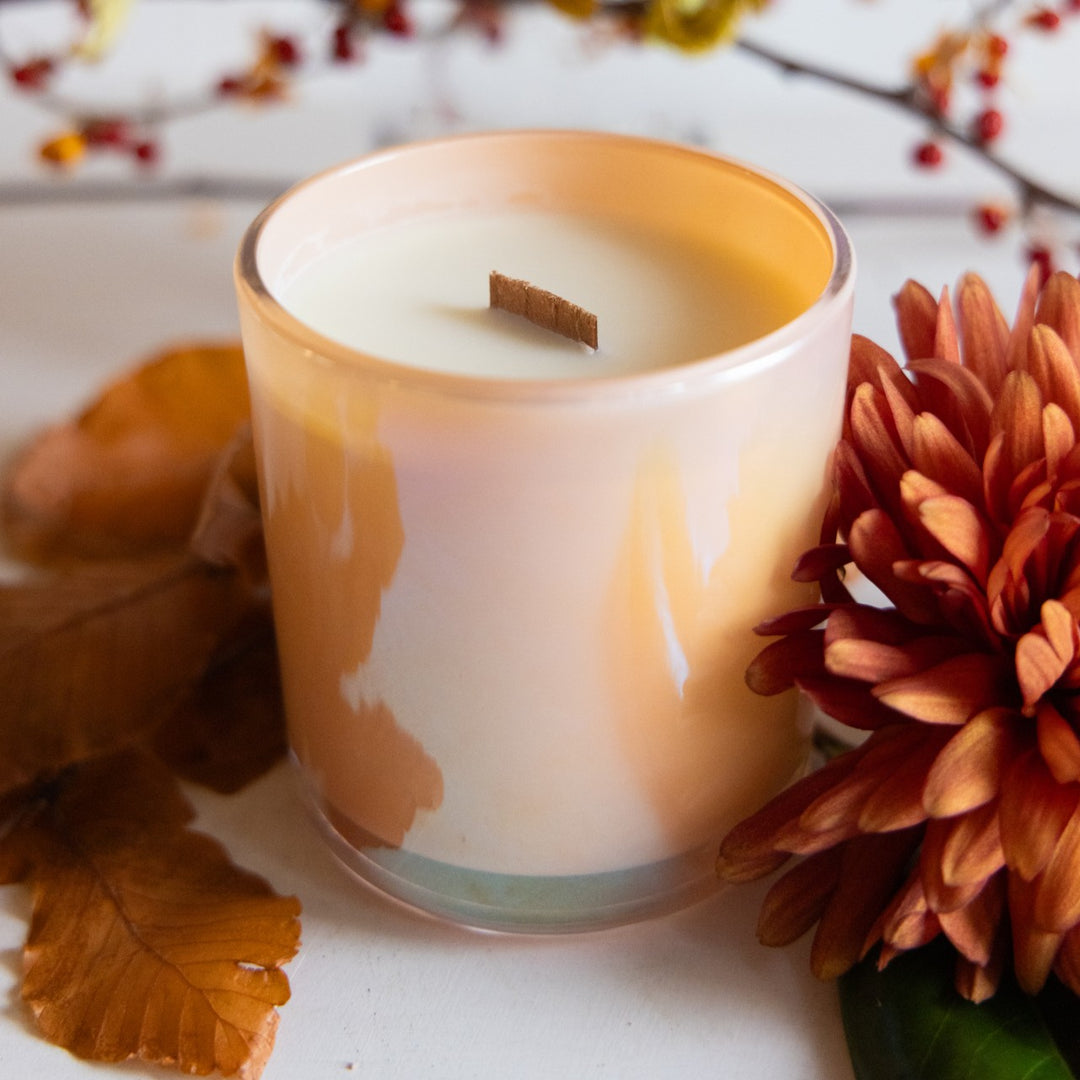 Candle in a glass jar with autumn leaves and flowers on a white surface
