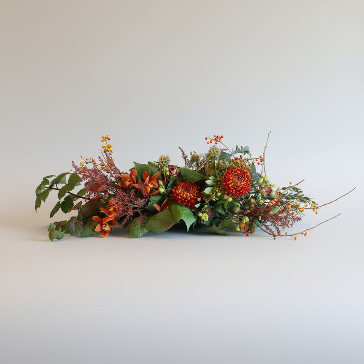 Autumn Centerpiece | A long and low arrangement perfect for your holiday table! Red, orange, and greens with berries and a variety of greenery. Photo taken against a white background.